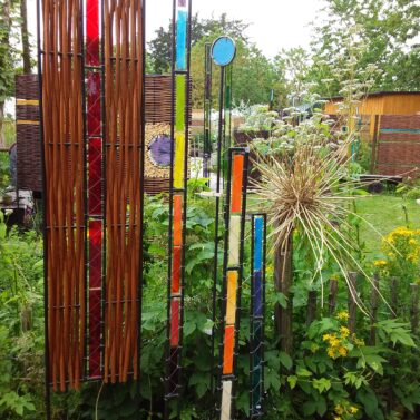 Glasstelen im Metallrahmen in einem blühenden grünen Garten